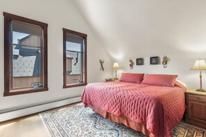 Une chambre avec un grand lit, deux fenêtres, une table de chevet, une lampe et un tapis.