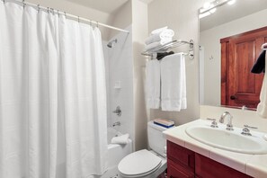 Une salle de bain avec un rideau de douche, des toilettes, un lavabo avec un miroir et un porte-serviettes avec des serviettes.