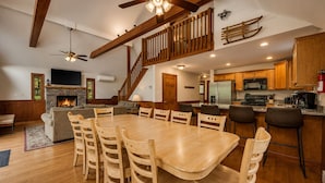 A spacious living area with a fireplace, wooden dining table, and a kitchen with modern appliances. - Arrowhead by PMR, 6 BR Lodge, Sleeps 16, Near Lake & Restaurants, Hot Tub (Lake Harmony)