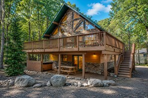 A cabin with a wooden deck, stone walls, and a staircase leading to a balcony.