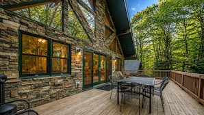 A stone cabin with a deck, outdoor seating, and a view of the forest. - Arrowhead by PMR, 6 BR Lodge, Sleeps 16, Near Lake & Restaurants, Hot Tub (Lake Harmony)