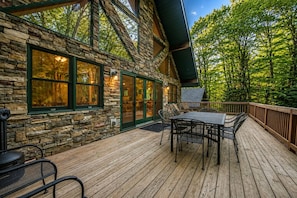 A stone cabin with a deck, outdoor seating, and a view of the forest.