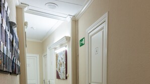 Un pasillo con piso de madera, una recepción con revistas, una puerta con número y un letrero de salida.