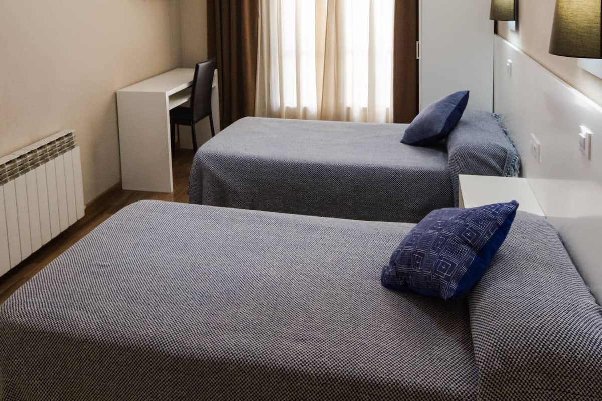 Habitación de hotel con dos camas, un escritorio, un televisor y una ventana con cortinas.