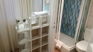 Un baño con ducha, inodoro y mampara de vidrio con espacios de almacenamiento.