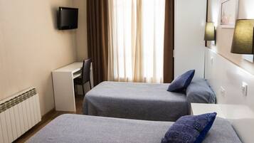 A hotel room with two beds, a desk, a chair, a TV, and a window with curtains.