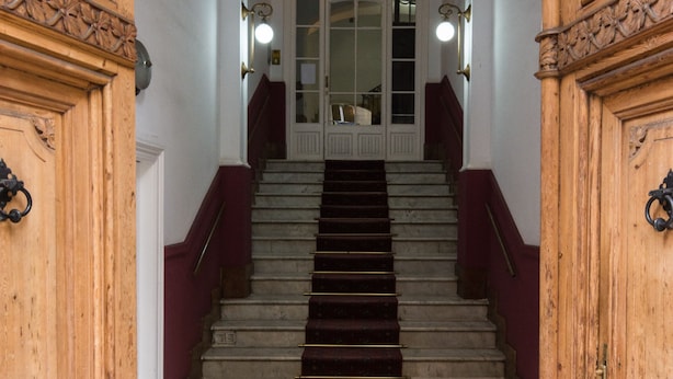 Una amplia escalera con alfombra roja que conduce a una puerta blanca con paneles de vidrio.