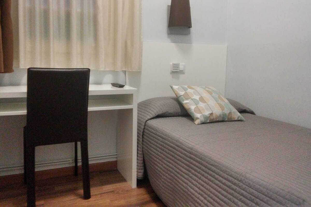 Un dormitorio pequeño y ordenado con una cama individual, un escritorio y una silla.