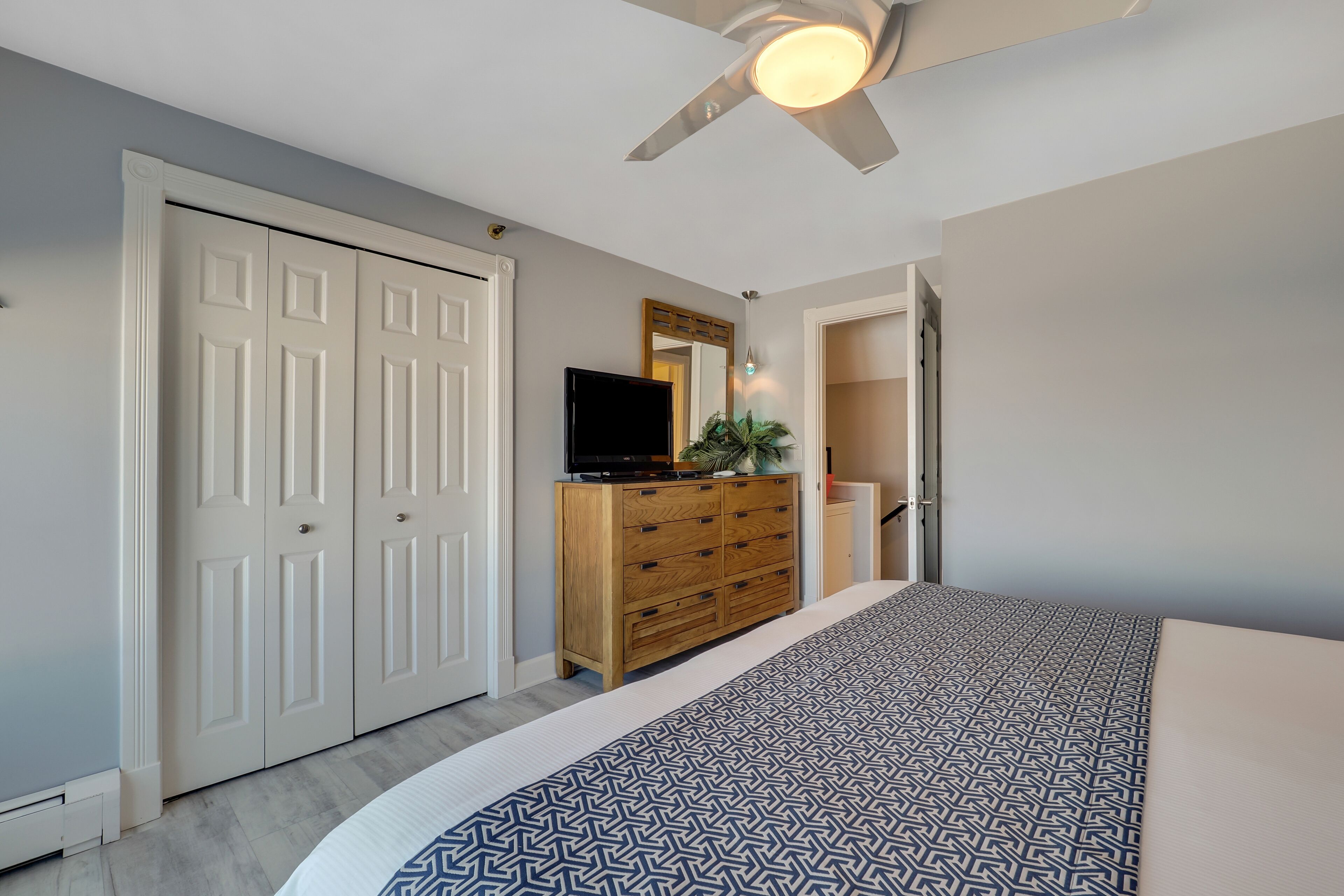 A bedroom with a bed, a dresser, a television, and a ceiling fan.