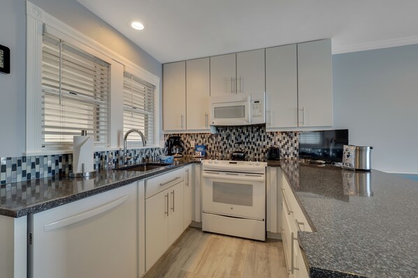 A modern kitchen with white cabinets, a microwave, a stove, and a coffee maker.