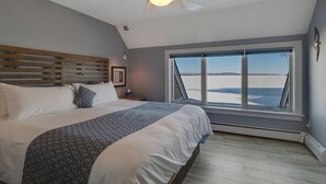 Un dormitorio con una cama grande, un ventilador de techo, una ventana con vista a la playa y un cabecero de madera.