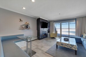 Un salon moderne avec une table basse en verre, un canapé, une cheminée et une grande fenêtre avec des rideaux.