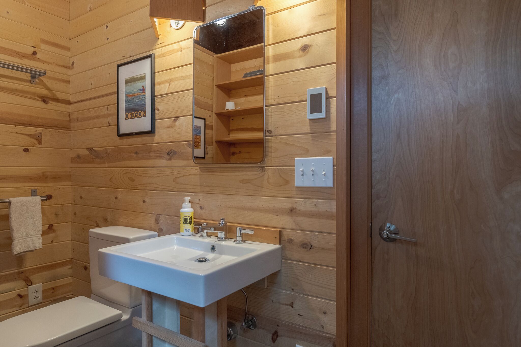 A wooden-paneled bathroom with a white sink, toilet, and mirror.