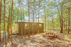 A cabin surrounded by tall trees, with a picnic table and a small deck area.