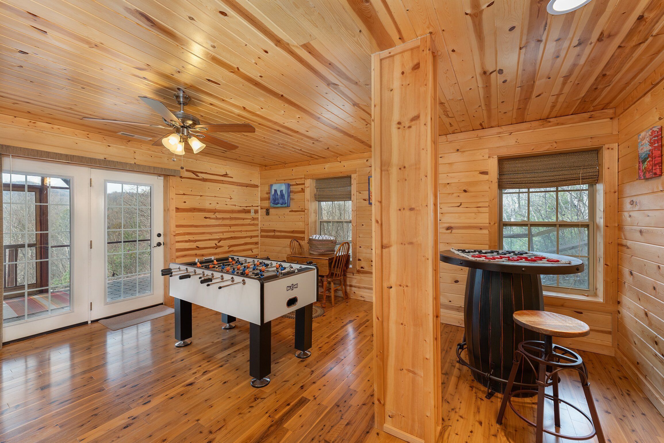 A wooden interior with a foosball table, a bar stool, and a ceiling fan.