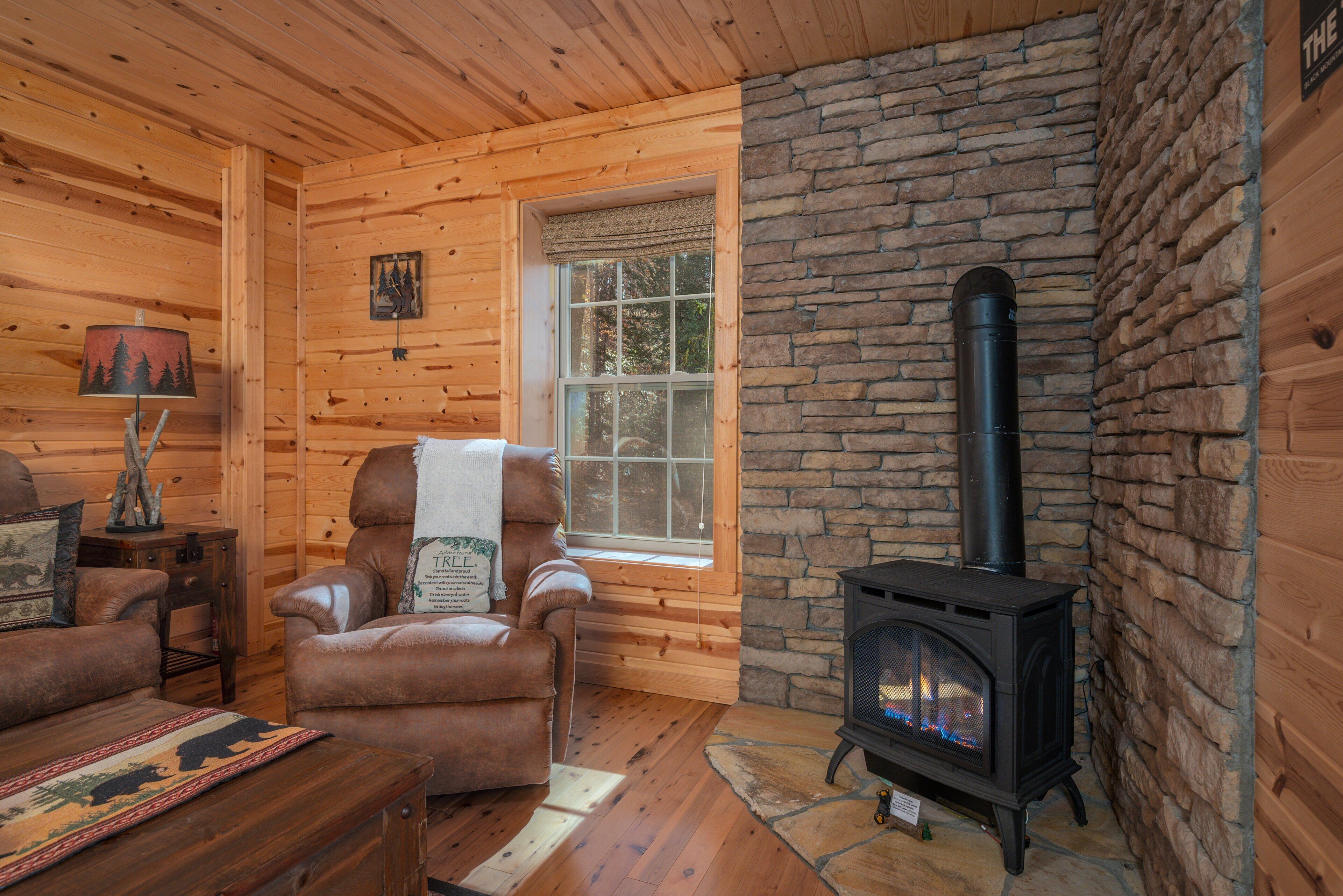 A cozy log cabin interior with a stone fireplace, a leather armchair, and a wooden floor.