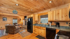 Een cabin interieur met houten wanden en vloeren, een bank, een eettafel en een keuken met een koelkast, fornuis en spoelbak.