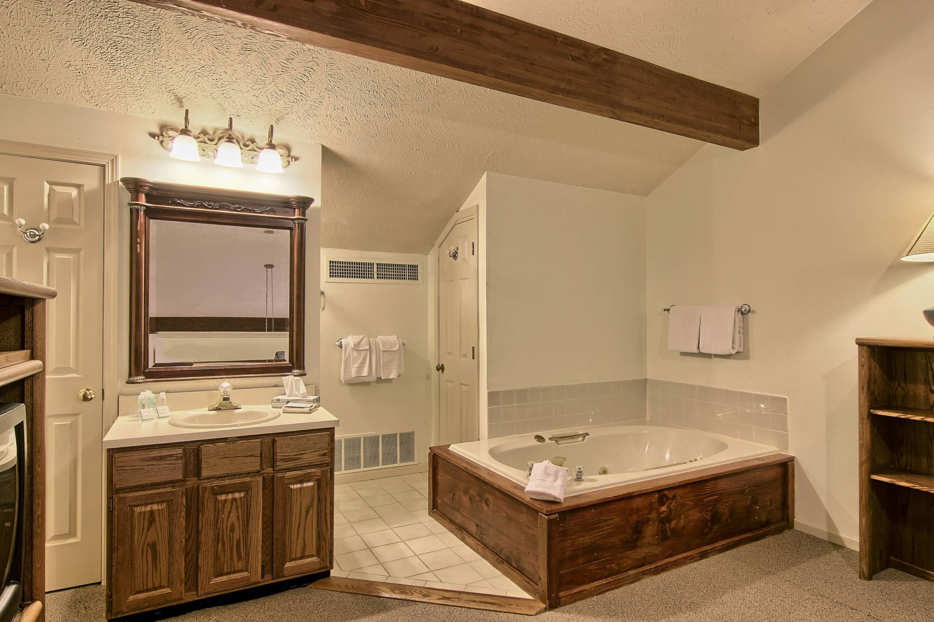 A bathroom with a wooden vanity, a large bathtub, and a mirror with lights.