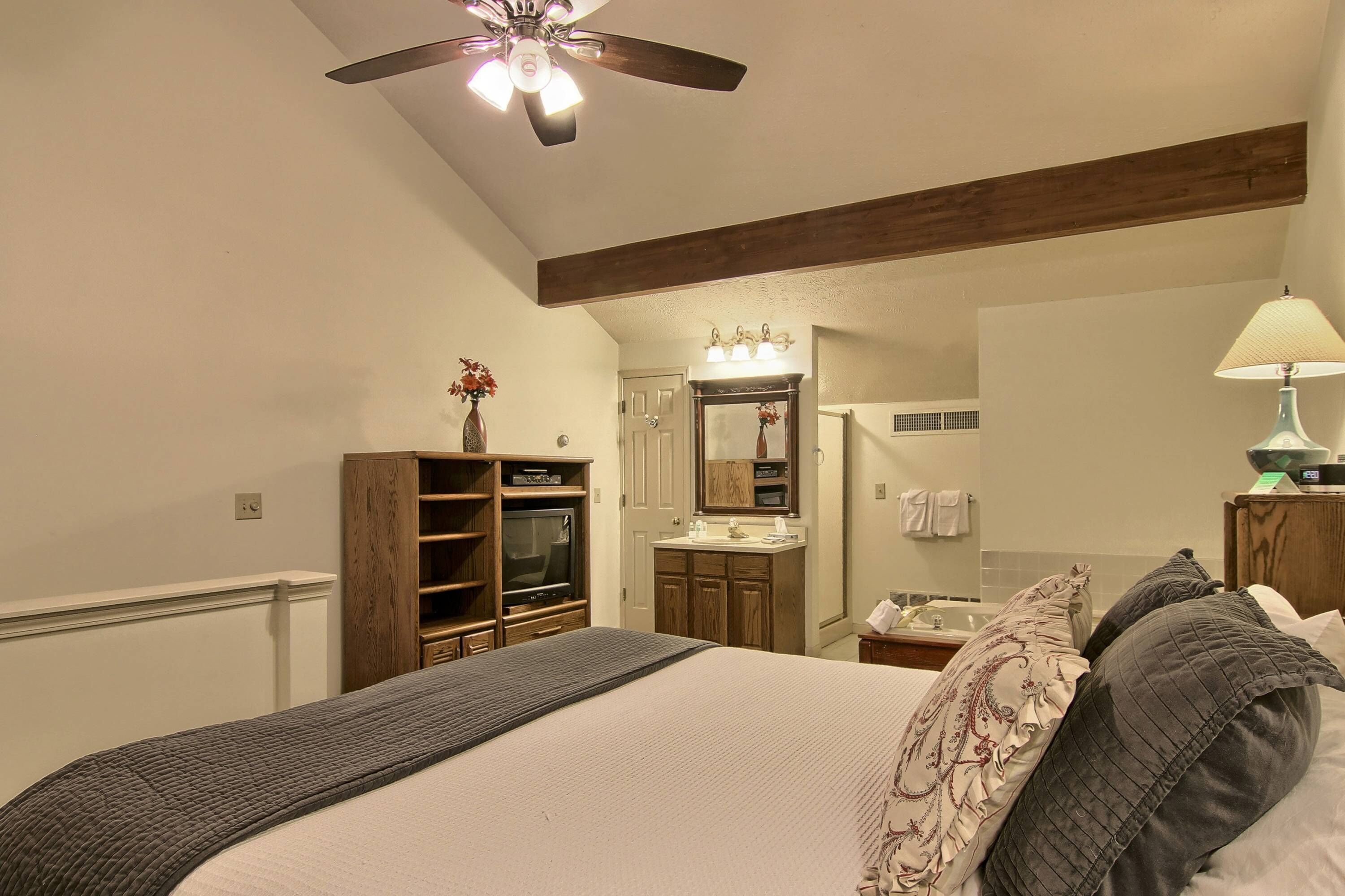 Un dormitorio con cama, ventilador de techo, tocador con espejo y televisor.