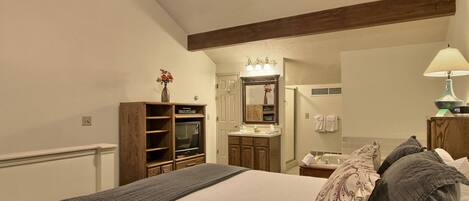 Un dormitorio con cama, ventilador de techo, tocador con espejo y televisor.