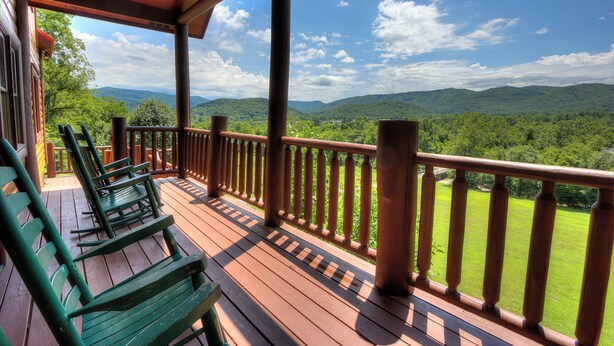 Una terraza de madera con sillas verdes y barandilla, con vista a un paisaje montañoso.
