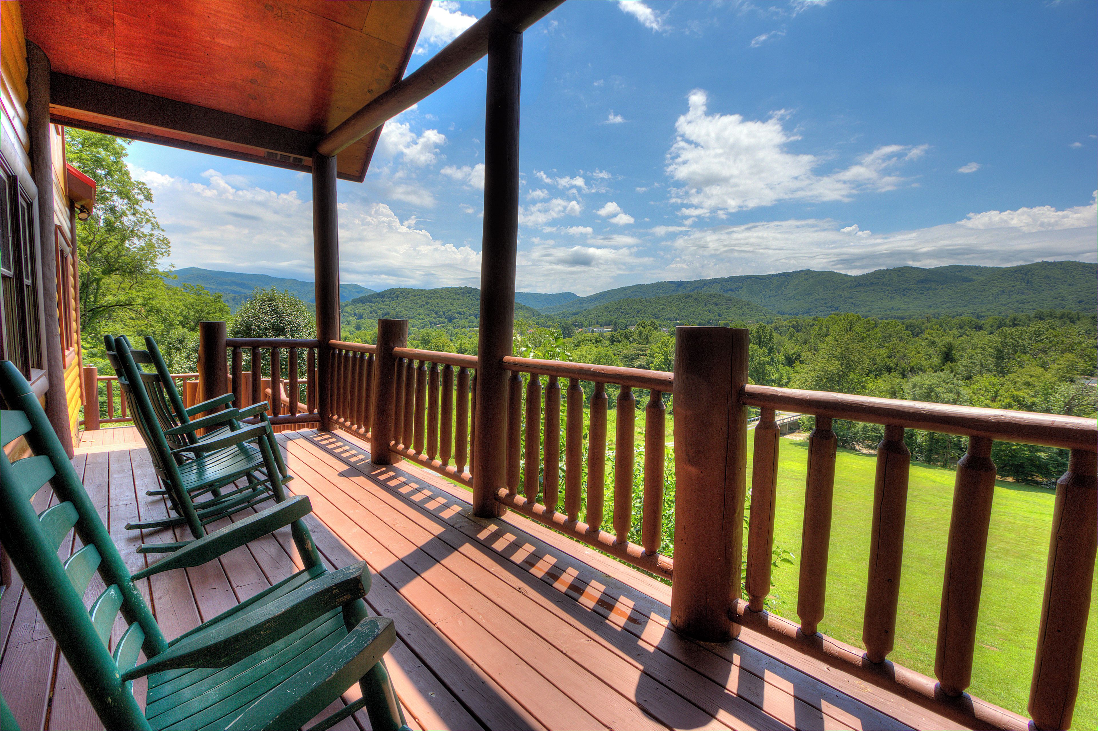 A wooden deck with a railing, green chairs, and a view of a mountainous landscape.