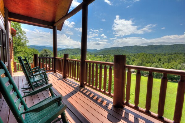 A wooden deck with a railing, green chairs, and a view of a mountainous landscape.