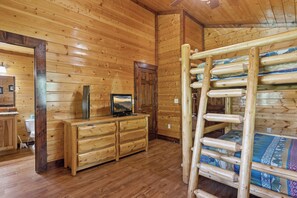 Interior de una cabaña de madera con una litera, un aparador de madera y un televisor.