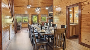 Una cabaña de madera con una larga mesa de comedor dispuesta para una comida, paredes de madera y una chimenea.