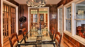 Un comedor con mesa de vidrio, sillas de madera, una araña y paneles de madera.