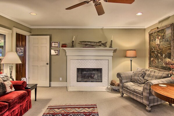 A living room with a fireplace, a red sofa, a plaid sofa, a wooden coffee table, and a patterned rug.