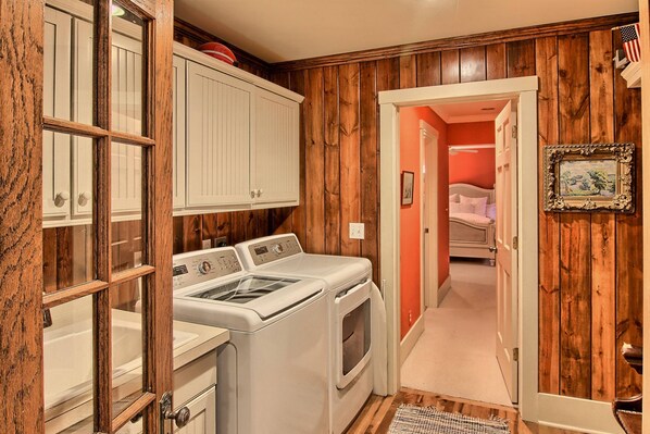 Un lavadero con lavadora y secadora, paredes de madera y un pasillo que conduce a un dormitorio.