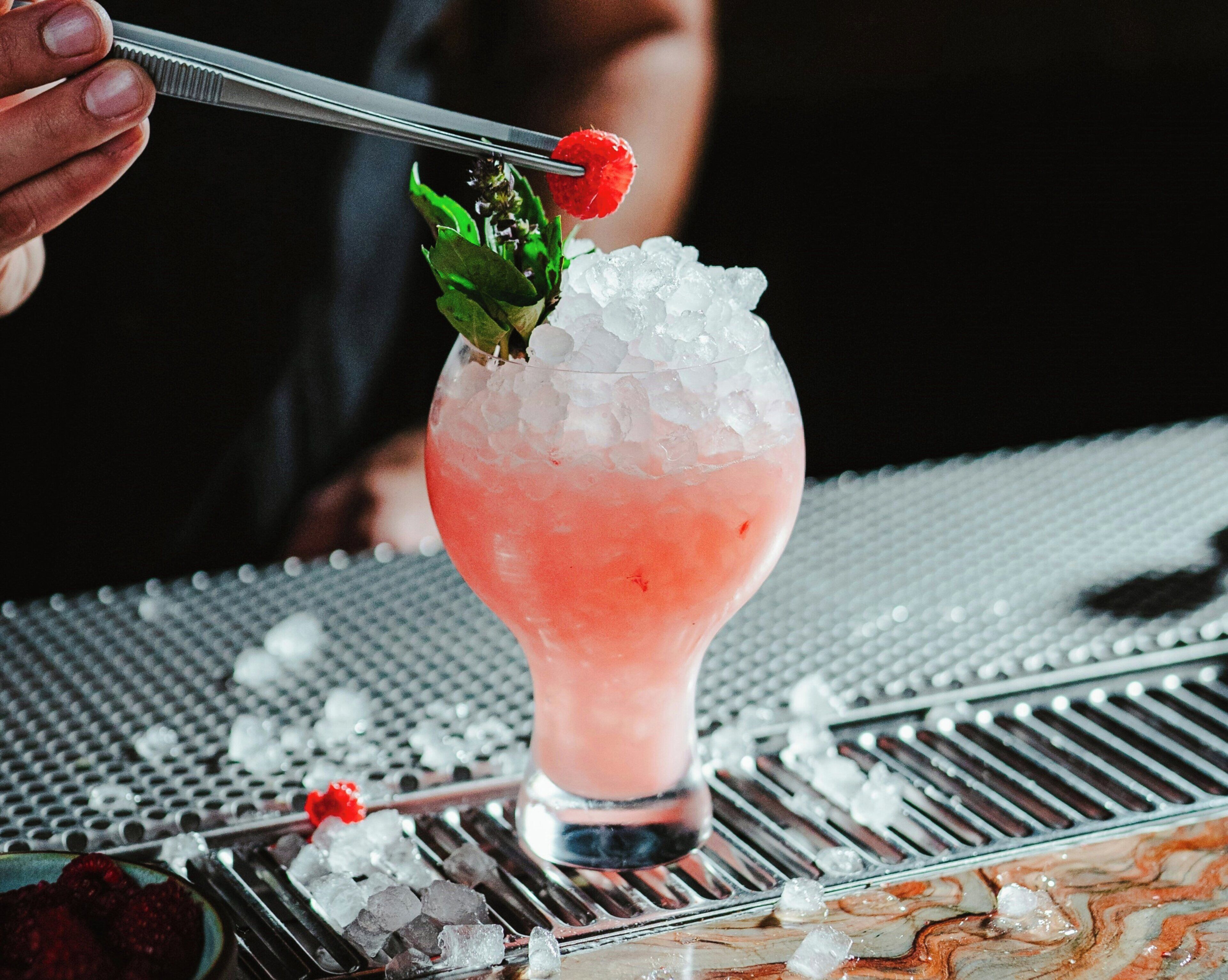A cocktail with ice and a strawberry garnish on a bar counter.