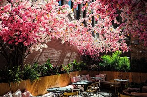 An outdoor seating area with tables and chairs, surrounded by a brick wall and flowering plants.