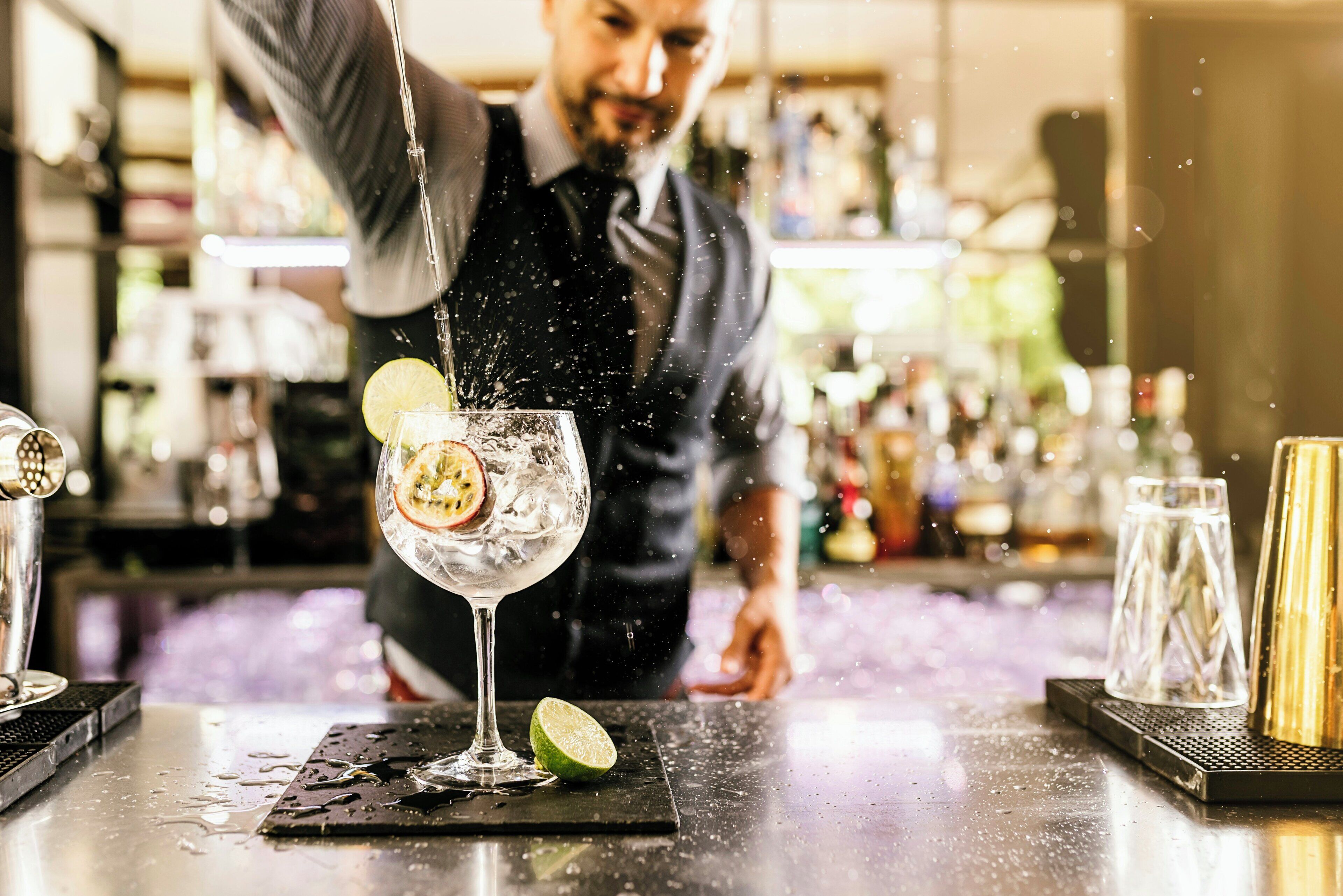 A bartender pouring a drink into a glass with a lime slice on the rim.