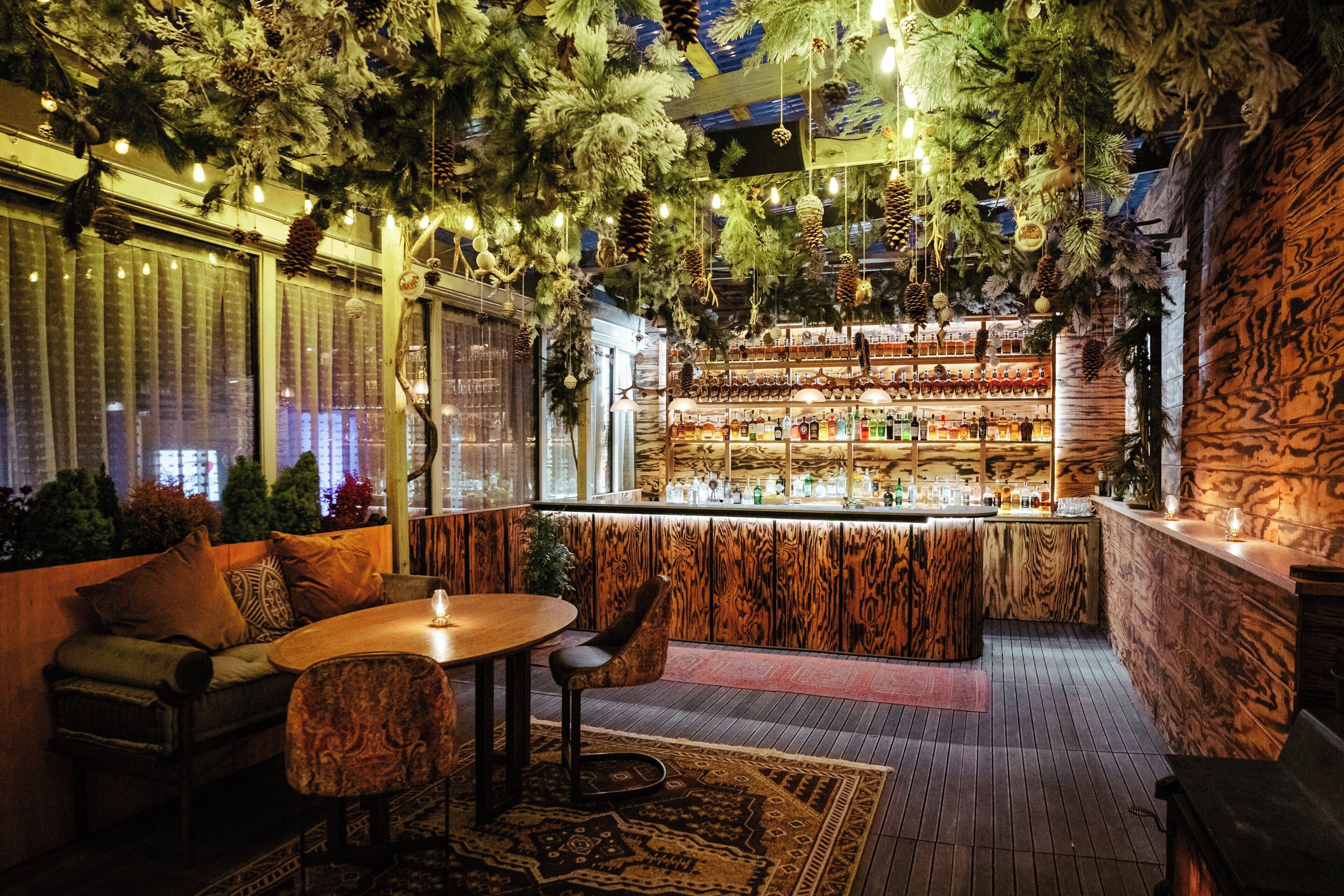 A bar area with a wooden bar counter, shelves of bottles, and hanging decorations.
