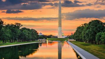 A large monument with a reflective pool in front, surrounded by trees and a clear sky.