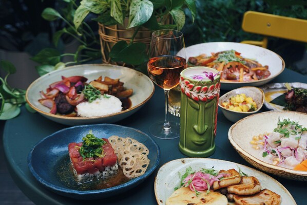 Una mesa servida con diversos platos, incluyendo sushi, una copa de vino y una bebida verde.