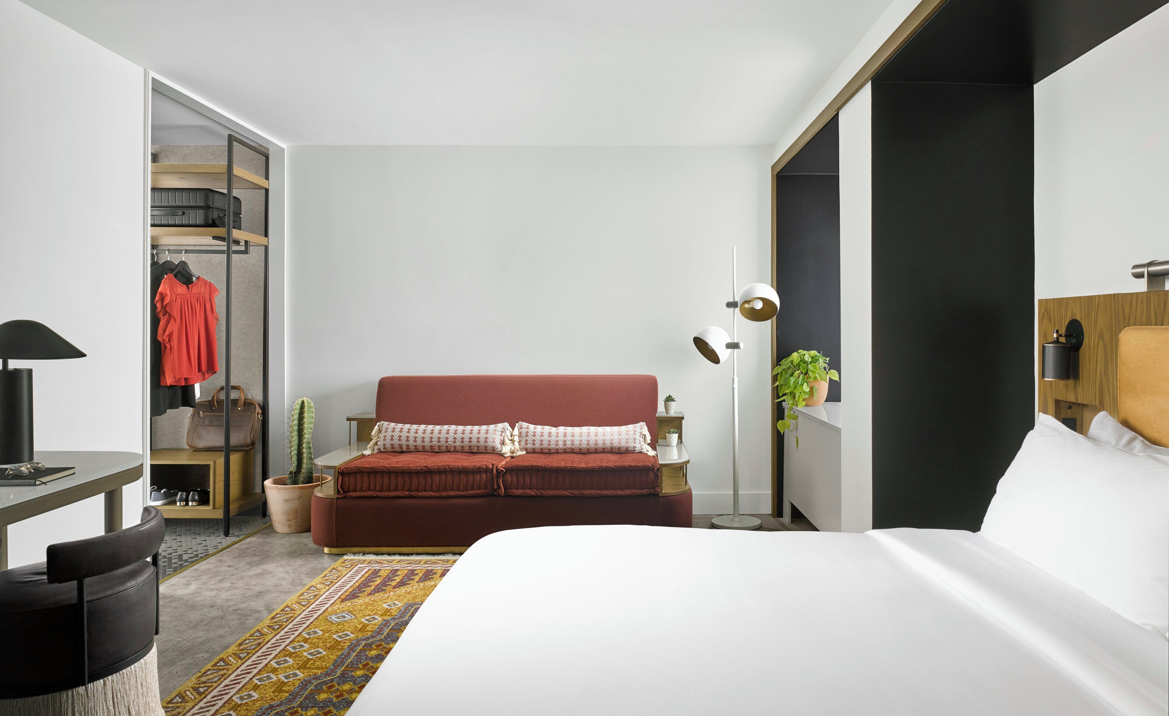 A modern bedroom with a bed, a red sofa, a wardrobe, and a small table with a lamp.