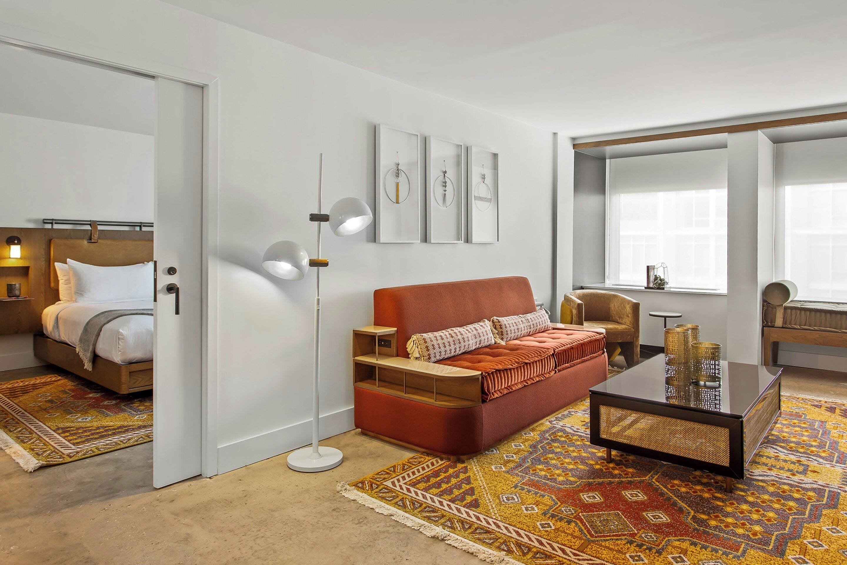 A modern hotel room with a bed, a sofa, a coffee table, and a large window.