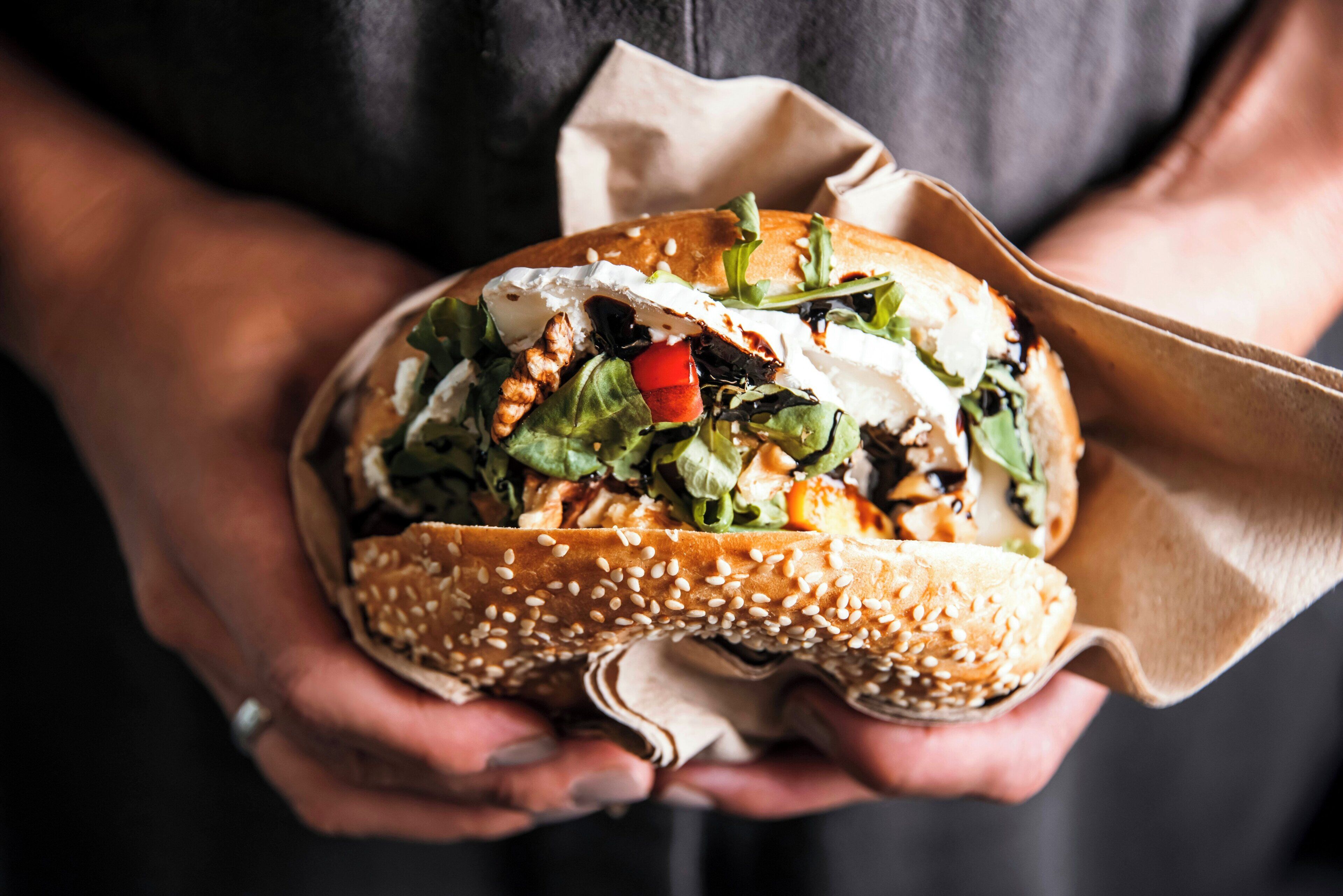 A person holding a sandwich with sesame seeds on the bread, wrapped in a paper.