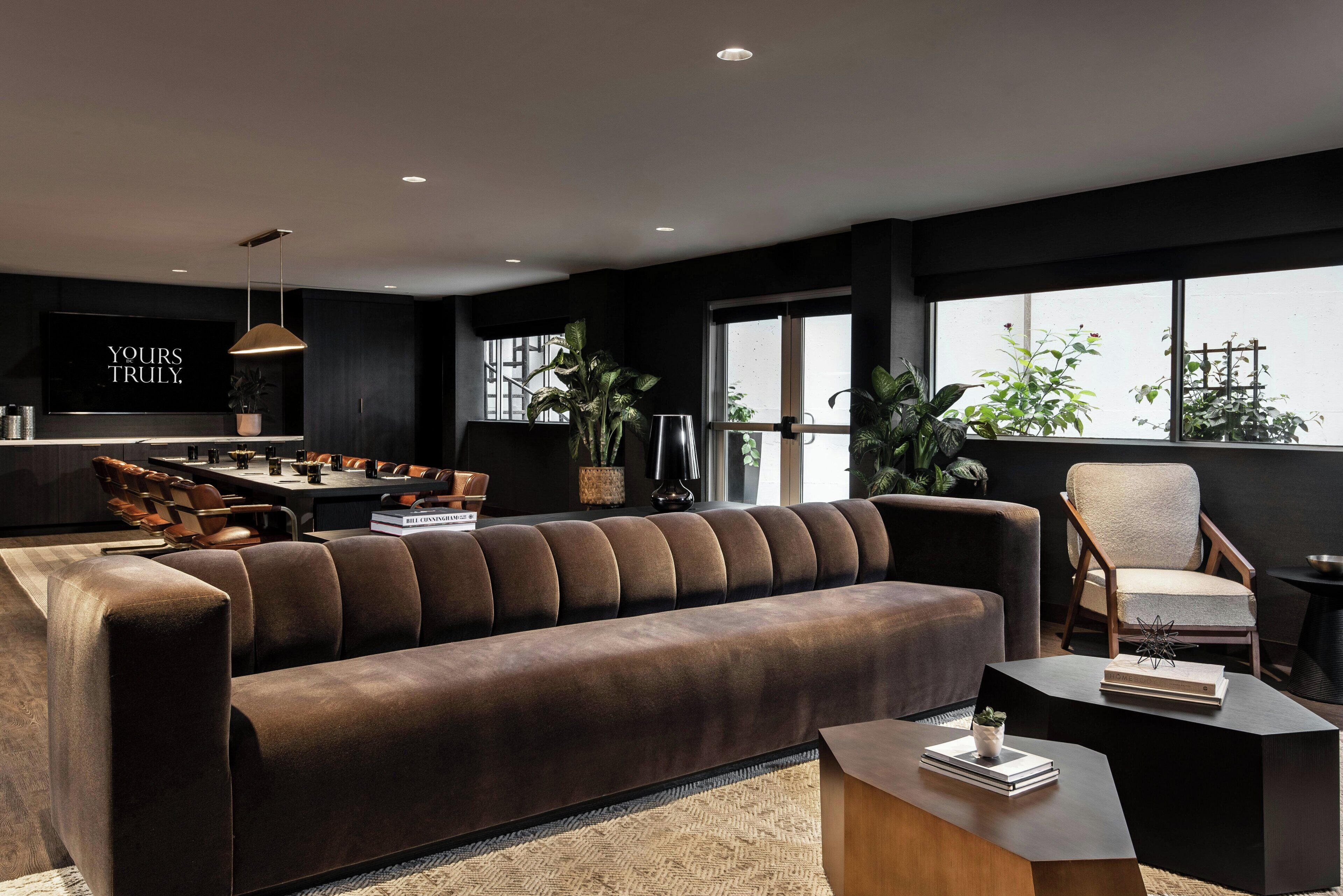 A modern living room with a large sofa, a dining area, and a television displaying 'YOURS TRULY.'
