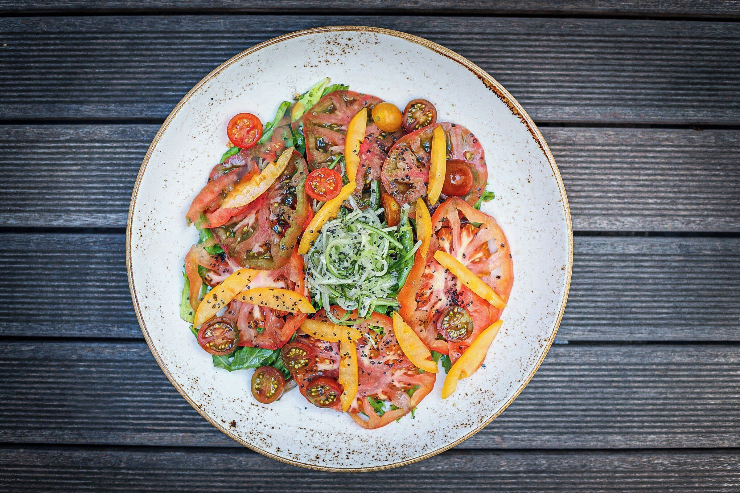 Een bord met plakjes tomaat, paprika en bladgroenten op een rustieke houten tafel.