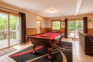 A pool table in a room with a sliding glass door leading to a deck, a sofa, and a framed picture on the wall.