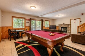 A pool table in a room with a fireplace, a television, and a dining area.