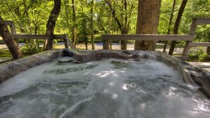 A hot tub surrounded by trees and a wooden deck.