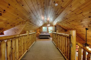 Een houten interieur met een schuine kap, een bed in het midden en een houten leuning langs de wanden.