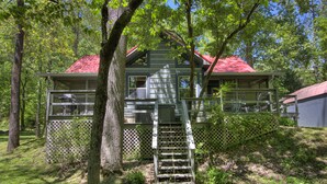 A cabin with a red roof, a wooden deck, and a ladder leading to the entrance.
