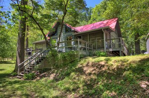 Een chalet met twee verdiepingen, een rood dak, een trap naar de bovenverdieping en een omliggend bebost gebied.