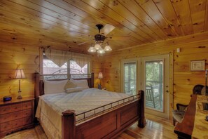 Een houten slaapkamer met een bed, bedlampen, een plafondventilator en een raam met gordijnen.